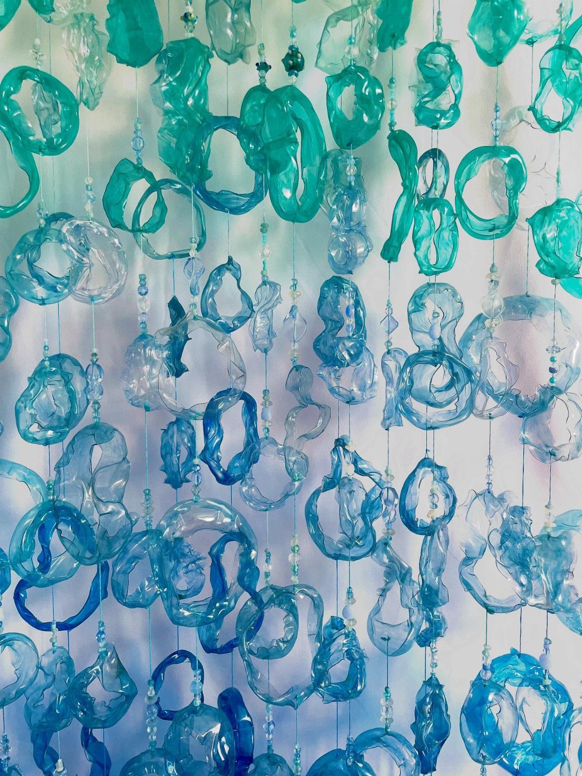 Hanging art installation made of melted blue and teal recycled plastic rings.